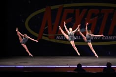 three young women are performing on stage with their arms in the air and one is holding her leg up