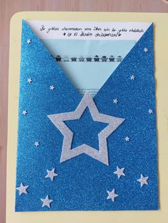 a blue envelope with silver stars on it and a white star in the middle, sitting on top of a wooden table