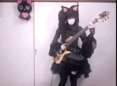 a woman wearing a black cat costume and holding a guitar while standing in front of a mirror