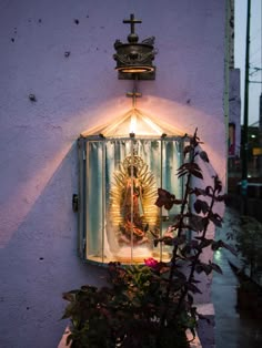 a small window with a statue on it next to plants and flowers in front of a purple wall