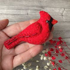 a small red bird sitting on top of a person's hand next to flowers