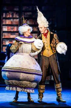 two people dressed in costumes standing next to each other on stage with bookshelves behind them