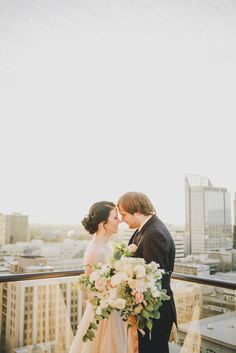 a bride and groom kissing on top of a building