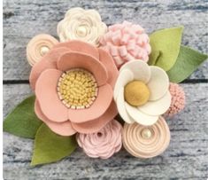 an arrangement of flowers made out of felt on a wooden surface with leaves and beads