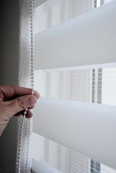 a hand is holding the blinds in front of a window with white beaded curtains