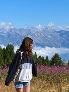 a woman is walking in the mountains with her back to the camera and looking at the sky