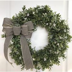 a wreath with black and white ribbons hanging on the front door, decorated with greenery