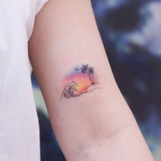 a woman's arm with a palm tree and wave tattoo on it