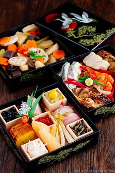 four black trays filled with different types of food on top of a wooden table