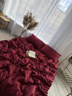 a red comforter on a bed next to a window