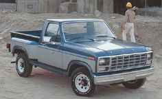 a blue pick up truck parked on top of a dirt field next to a construction worker