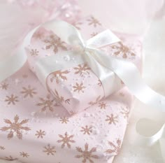 a pink gift box with white ribbon and snowflakes on the wrapping paper next to it