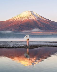 a person standing in front of a body of water with a mountain in the background