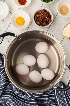 eggs are being cooked in a pot with other ingredients around it on a white wooden table