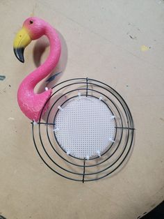 a pink flamingo sitting on top of a wire rack next to a white circle