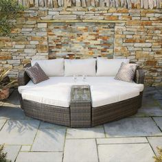 an outdoor couch with pillows on it in front of a stone wall and planter