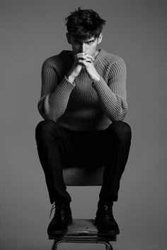 a black and white photo of a man sitting on a chair with his hands clasped