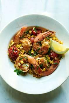 a white bowl filled with shrimp, corn and garnish on top of a table