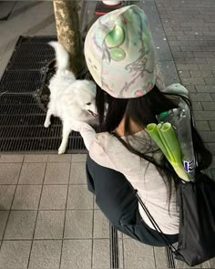 a woman sitting on the ground holding a white dog and flowers in her lap while wearing a hat