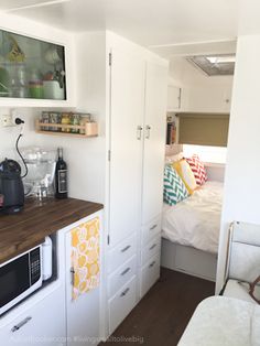 a small kitchenette with white cabinets and wood counter tops, along with a bed in the background