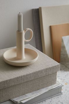 a white candle sits on top of a stack of books next to a cup and saucer