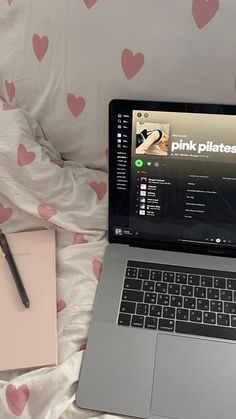 an open laptop computer sitting on top of a bed next to a notebook and pen