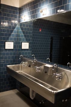 a bathroom sink with two faucets in front of a blue tiled wall and mirror