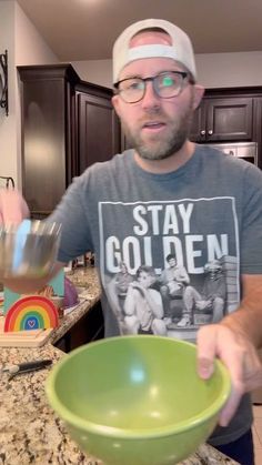 a man holding a green bowl in his hand while standing next to a kitchen counter