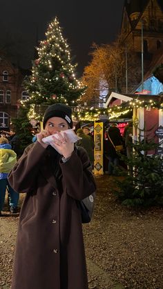 a man standing in front of a christmas tree holding a napkin to his mouth with both hands