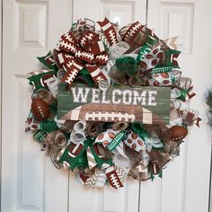 a football wreath with the word welcome is hanging on a white door, decorated with green and brown items