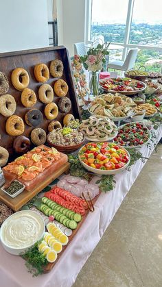 an assortment of donuts and other food items on a long table in front of a large window