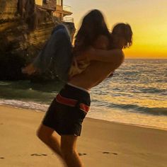 a man and woman running on the beach at sunset with an ocean in the background