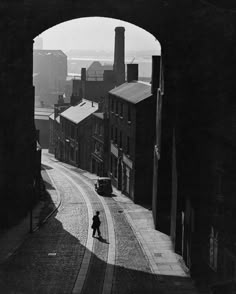 black and white photograph of a person walking down an alleyway with buildings in the background