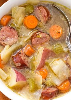 a close up of a bowl of soup with carrots and meat in it on a table