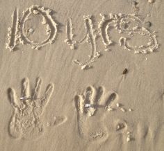 the word joy written in sand with two handprints and an animal's paw