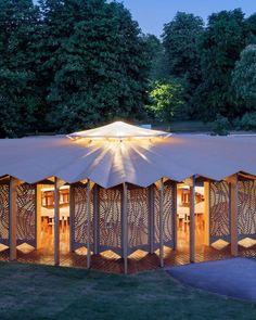 a large tent is lit up at night in the middle of a grassy area with trees