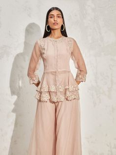 Editor's Note Blush scallop flora peplum and sharara is an elegant ethnic wear set, made of lightweight organza fabric. The peplum top features a beautiful floral embellishment and a scallop hemline. The set includes a pair of sharara pants with a flared silhouette. Color: Blush Fabric: Organza Component: Peplum and sharara Occasion: Cocktail and wedding guest Embroidery: Floral hand & machine embellishment Disclaimer: Product color may slightly vary due to photographic lighting sources or your Organza Peplum Sharara For Festive Occasion, Diwali Embellished Peplum Sharara, Elegant Sharara With Floral Embroidery And Peplum, Elegant Floral Embroidered Sharara With Peplum, Elegant Floral Embroidered Peplum Sharara, Blush Fabric, Sharara Pants, Floral Embellishment, Dresses Traditional