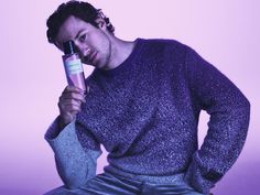 a man sitting on a stool holding a hair dryer in his hand and looking at the camera