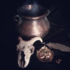 an old metal pot sitting on top of a table next to a feather and skull