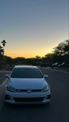 a white car is parked on the side of the road at sunset with palm trees in the background