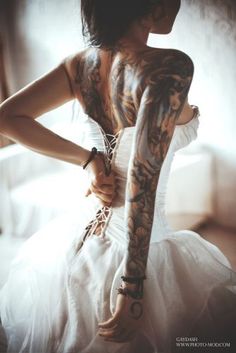 a woman with tattoos on her arms and arm is holding onto a white dress while sitting in front of a window