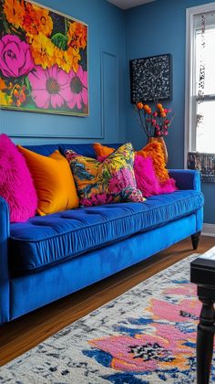 a blue couch with colorful pillows on it in front of a large painting and window