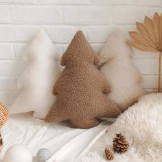 three pillows with different shapes and sizes on top of a white blanket next to two pine cones