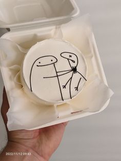 a person holding up a small cake in a box with an image of two people on it