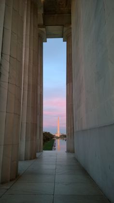 the washington monument is seen through an archway at dusk with pink skies in the background