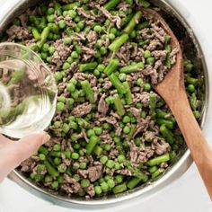 a person is pouring water into a pot filled with meat and asparagus on the side