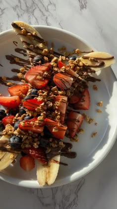 a white plate topped with sliced bananas and strawberries on top of a marble table