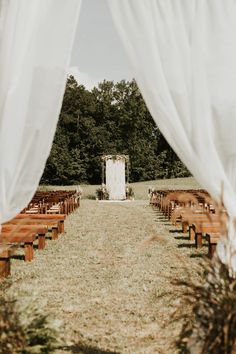 an outdoor ceremony with wooden benches and white drapes