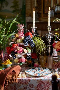 a table topped with plates covered in fruit and veggies next to two candles