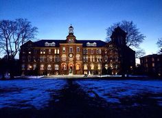 an old building lit up at night with snow on the ground and trees in front